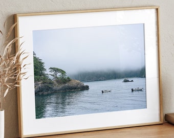 May include: A framed photograph of a foggy landscape with a small island and boats in the distance. The frame is light wood and the photo is printed on white paper.