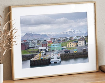 May include: A framed photograph of a colorful town with snow-capped mountains in the background. The town is located on a waterfront with boats docked at the pier.