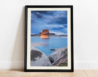 May include: A framed photograph of a large rock formation rising from a blue lake. The sky is cloudy and the water is calm. The rock is a reddish-brown color and the water is a light blue.