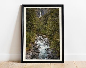 May include: A framed photograph of a waterfall cascading down a rocky mountainside, surrounded by lush green trees. The water flows into a stream that winds its way through the forest.