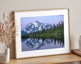 May include: A framed photograph of a mountain range reflected in a still lake. The mountain peaks are snow-capped and the sky is a soft blue with a hint of pink.