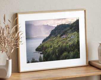 May include: A framed photograph of a scenic landscape with a lake, mountains, and lush green trees. The photo is displayed on a wooden shelf with a vase and a basket.