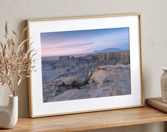 May include: A framed photograph of a desert landscape with a mountain range in the distance. The photo is in a light wood frame and is hanging on a wall.