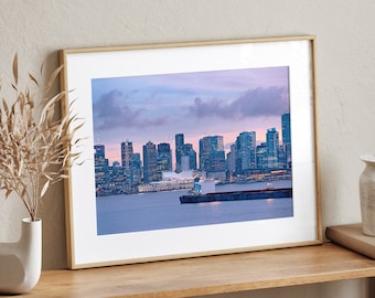 May include: A framed photograph of a city skyline at dusk with a large ship in the foreground. The city is lit up with lights and the sky is a soft purple color.