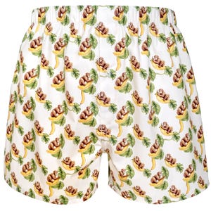 May include: White boxer shorts featuring an all-over repeating pattern of brown monkeys sitting on yellow bananas surrounded by green tropical leaves. The garment has an elasticated waistband and a central button fly closure on the front.