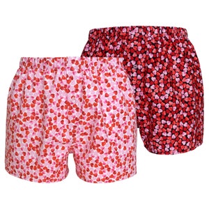 May include: Two pairs of boxer shorts with a heart print. One pair is pink with red hearts and the other is black with red and pink hearts.