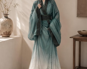 May include: A floor-length dress featuring a teal and white gradient color scheme. The garment has long, wide sleeves with dark green patterned trim, a matching wide waistband, and a sheer overlay with a subtle bamboo leaf print at the hem.