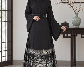 May include: A black long-sleeved dress with a wrap-style bodice and a wide waistband. The floor-length skirt features a detailed hemline pattern in white, green, and silver, depicting intricate dragon motifs and floral elements along the bottom.