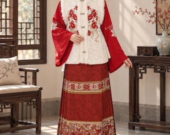 May include: A red long-sleeved garment with a white faux fur vest featuring floral embroidery, worn over a long red skirt with intricate gold and red patterned borders at the hem and waist, creating a layered ensemble.