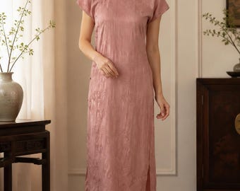 May include: A dusty rose midi-length cheongsam dress featuring a mandarin collar, short cap sleeves, and a subtle tonal floral jacquard pattern. The garment includes a side slit and traditional knot button closures along the upper right chest.