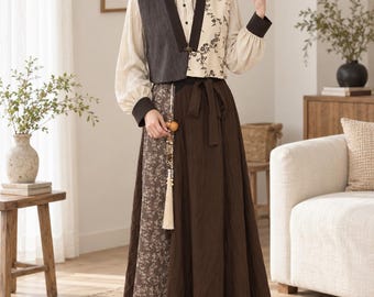 May include: A long-sleeved blouse featuring a dark gray vest-style overlay on one side and a cream-colored floral pattern on the other, paired with a floor-length skirt that combines a solid dark brown panel with a brown floral print panel.
