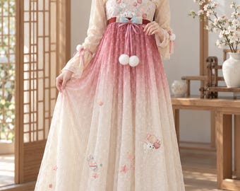 May include: A floor-length dress featuring a cream-colored bodice with a square neckline and long, sheer sleeves. The skirt transitions from a deep pink at the waist to a light cream at the hem, decorated with small embroidered rabbits and strawberries.