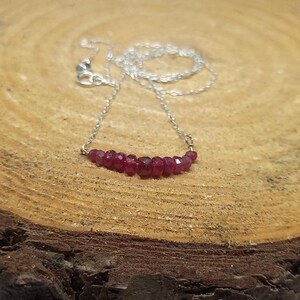 May include: A silver chain necklace with a delicate row of small, faceted, ruby red gemstones.