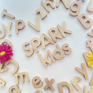 May include: Wooden alphabet letters in a circular pattern on a white background. The letters spell out "SPARK kids".