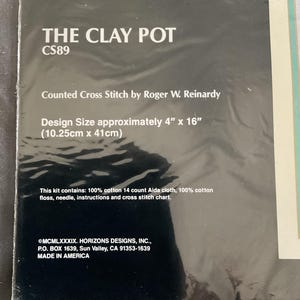 May include: A cross-stitch kit titled "The Clay Pot" by Roger W. Reinardy. The design size is approximately 4" x 16" (10.25cm x 41cm). The kit includes 100% cotton Aida cloth, floss, a needle, instructions, and a cross-stitch chart.