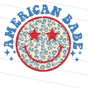 May include: A blue and yellow smiley face with red stars for eyes and the words "American Babe" in blue around it. The smiley face has a distressed, vintage look.