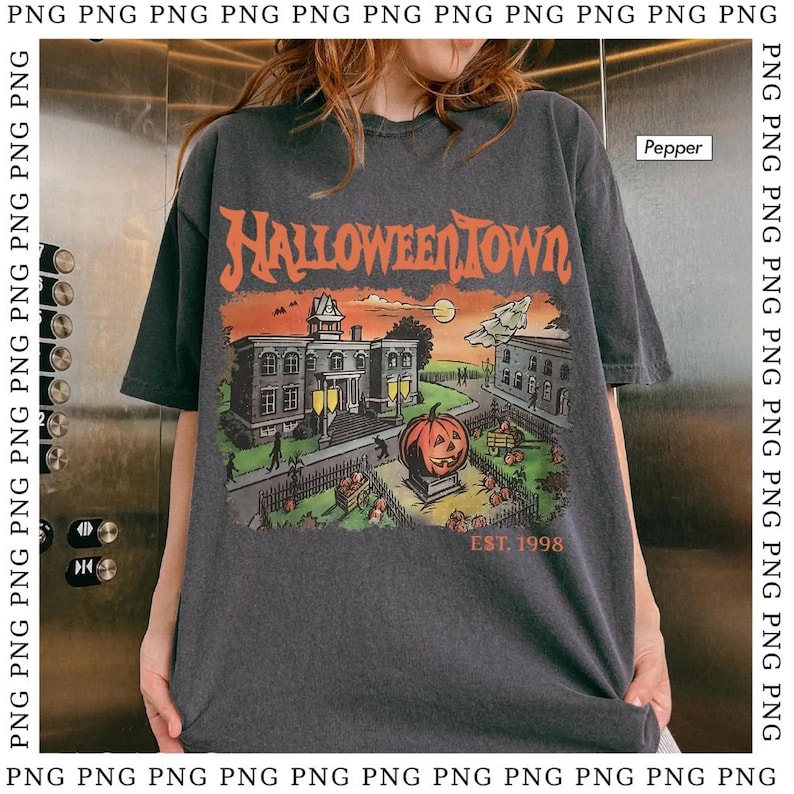 May include: Dark gray t-shirt with a Halloween-themed graphic. The design features a pumpkin, buildings, and the text "HALLOWEEN TOWN EST. 1998" in orange and white. The shirt has short sleeves.