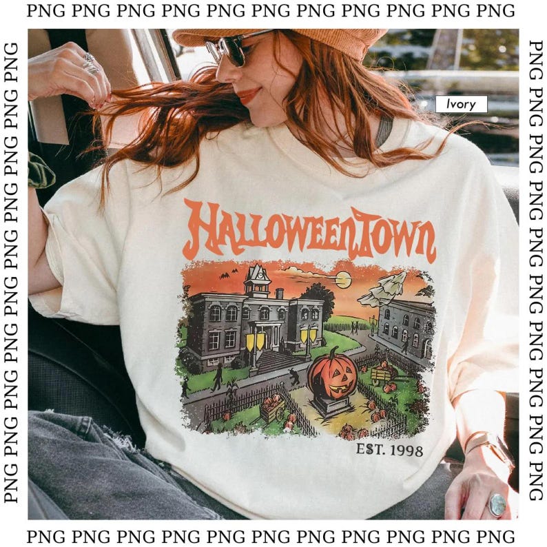 May include: Ivory-colored t-shirt with a Halloween-themed graphic. The design features the words "Halloween Town" in orange, along with a spooky town scene, a jack-o'-lantern, and the text "EST. 1998".