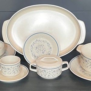 May include: A set of beige and blue floral patterned ceramic dishes, including a large oval serving platter, a small bowl, a cup and saucer, and a covered dish with a handle.