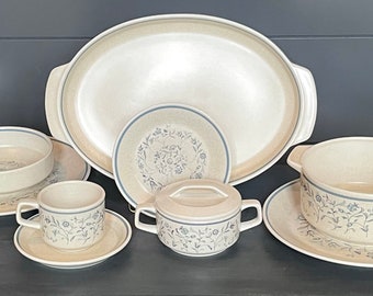 May include: A set of beige and blue floral patterned ceramic dishes, including a large oval serving platter, a small bowl, a cup and saucer, and a covered dish with a handle.