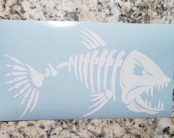 May include: White vinyl decal of a fish skeleton with a menacing expression. The fish has a large mouth with sharp teeth and a detailed skeletal structure.