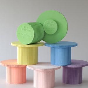 Puede incluir: Seis soportes redondos para tartas de colores vivos con bordes acanalados. Los soportes están hechos de un material texturizado y están disponibles en amarillo, azul claro, melocotón, rosa, lavanda y verde. El soporte verde tiene una etiqueta que dice "Prop Options 8" Top Plate Base 5" Use for 11" or less 1" Base".