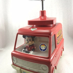 Può includere: Un camioncino dei gelati rosso giocattolo con una figura di Topolino al volante. Il camioncino ha una manovella in cima e un cartello che dice "Mickey's Ice Shop".