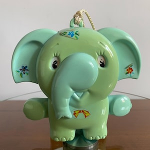 May include: A light green plastic elephant toy with a blue trunk and colorful flower stickers. The toy has a pull string and is designed for babies.