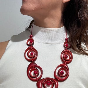 May include: A red statement necklace with large, round, concentric circles and small red beads. The necklace is made of wood and has a natural, organic look.