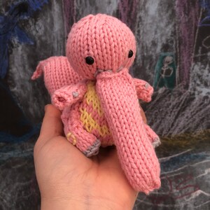 Op de afbeelding: Een roze gebreid speelgoed met een lange snuit en een geel en roze patroon op het lichaam. Het speelgoed heeft zwarte ogen en een gestikte glimlach.