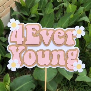 May include: A pink and brown cake topper with the text "4Ever Young" and white daisies.