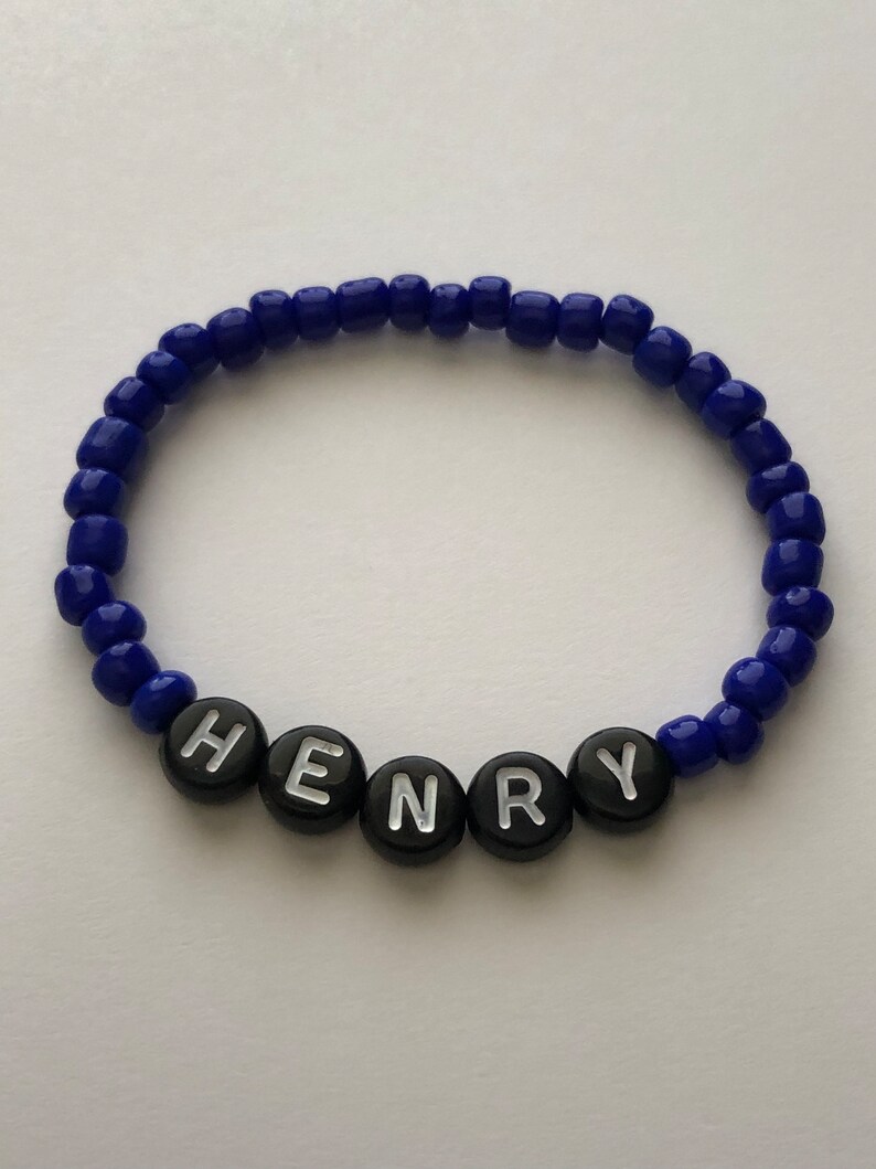 Pu&ograve; includere: Un braccialetto di perline blu con perline a forma di lettera nere che compongono il nome "HENRY".