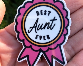 May include: Pink and white sticker with a gold outline. The sticker is shaped like a ribbon and says "Best Aunt Ever" in black text.