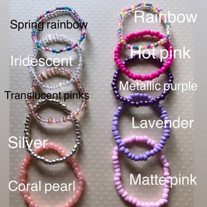 May include: A set of ten colorful beaded bracelets, including rainbow, hot pink, iridescent, metallic purple, translucent pinks, lavender, silver, and coral pearl. The bracelets are arranged vertically in a row, with the names of each color written below them.