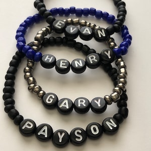 Pu&ograve; includere: Cinque braccialetti neri con perline e lettere bianche che compongono i nomi Evan, Henry, Gary e Payson.