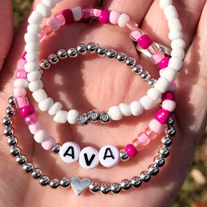 May include: Three beaded bracelets with a silver heart charm and the name "AVA" spelled out in silver beads.