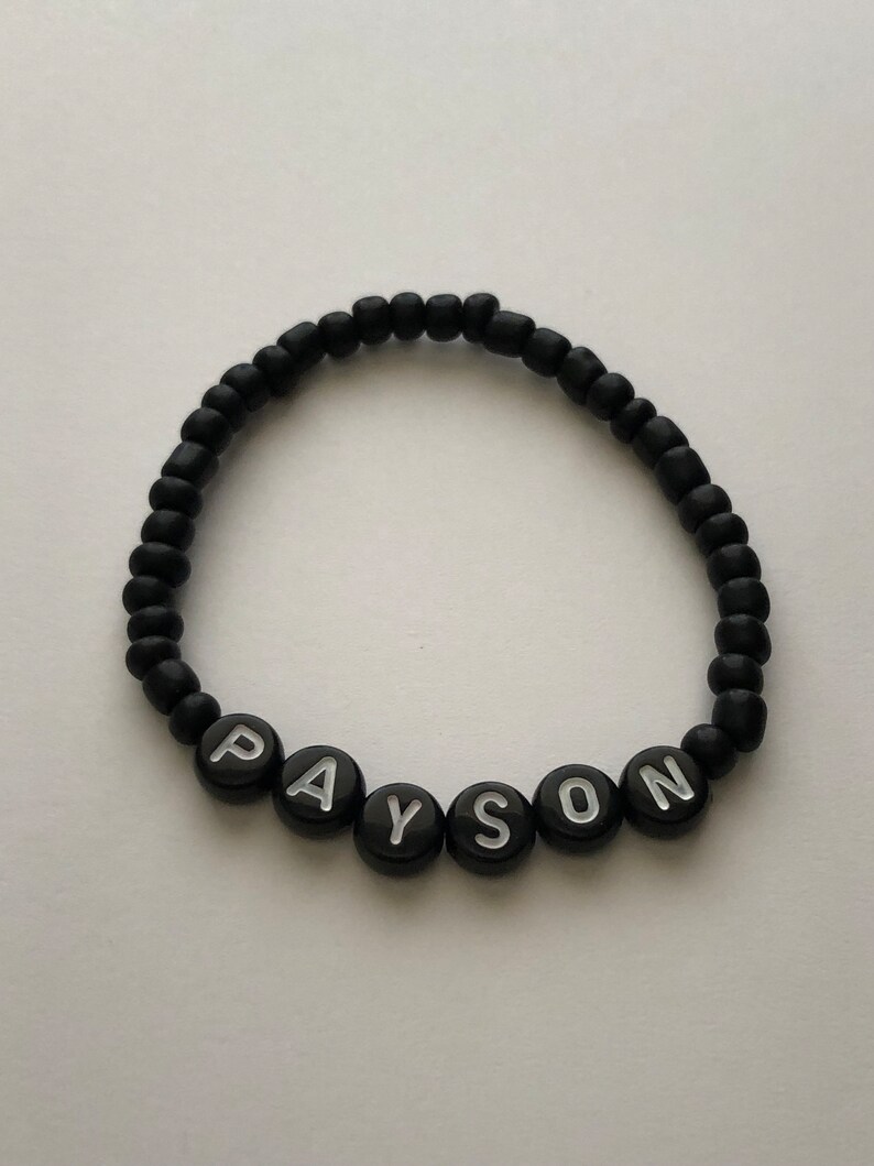 Pu&ograve; includere: Braccialetto di perline nere con il nome "PAYSON" scritto in lettere bianche.