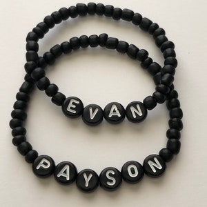 Pu&ograve; includere: Due braccialetti neri con perline con i nomi "Evan" e "Payson" scritti in lettere bianche.