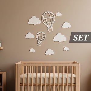 Könnte beinhalten: Wanddekoration für das Kinderzimmer mit weißen Heißluftballons und Wolken-Ausschnitten. Das Set enthält zwei Heißluftballons und mehrere Wolken, angeordnet an einer neutralfarbenen Wand über einem Holzbett. Der Text "SET 1" wird in einem grauen Rechteck angezeigt.