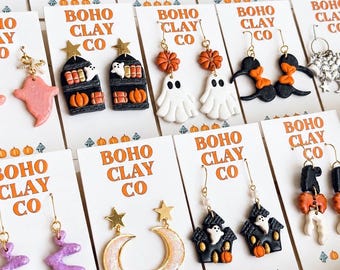 May include: A collection of polymer clay earrings displayed on white cards labeled Boho Clay Co. The designs feature Halloween themes including white ghosts, black coffins, orange pumpkins, black cauldrons, crescent moons, and stars with various metal hooks.