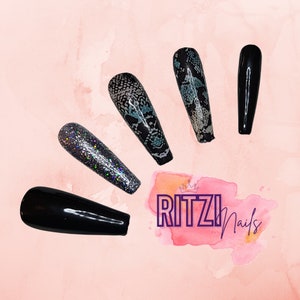 May include: Five long, black press-on nails with different designs. One nail has a black glitter finish, one has a black and white snake skin pattern, one has a black and blue snake skin pattern, and two are solid black.