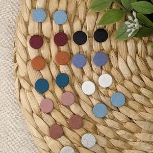 May include: Assortment of 18 small round stud earrings in various colors, including red, blue, green, brown, pink, and white. The earrings are displayed on a woven straw mat.