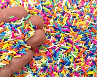 May include: A close-up of a large quantity of colorful sprinkles. The sprinkles are long and thin, and they are in a variety of colors, including red, orange, yellow, green, blue, and purple.