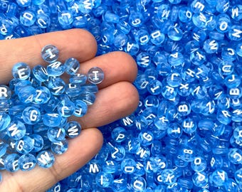 May include: A handful of blue translucent alphabet beads with white letters. The beads are round and have a smooth surface.