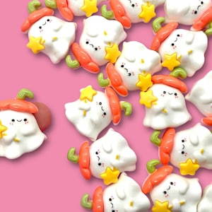 May include: A collection of small, white ghost-shaped charms with orange pumpkin tops and yellow star accents. The charms are made of polymer clay and have a cute, cartoon-like appearance.