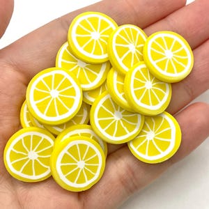 May include: A pile of yellow lemon slice shaped polymer clay charms. The charms are about 1 inch in diameter and have a white outline.