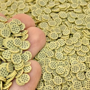 May include: A close-up of a pile of small, light brown cookie-shaped sprinkles with black chocolate chips. The sprinkles are perfect for decorating cakes, cupcakes, and other desserts.