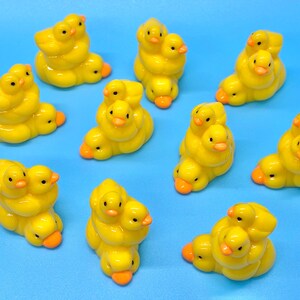 May include: A collection of yellow duckling figurines with orange beaks and black eyes. Each figurine features multiple ducklings clustered together. The background is a solid light blue.