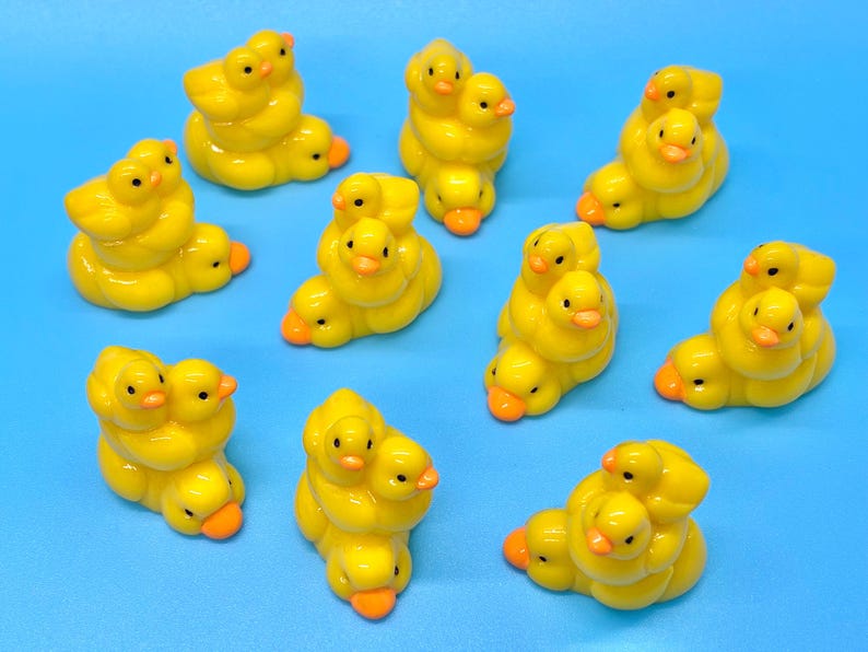 May include: A collection of yellow duckling figurines with orange beaks and black eyes. Each figurine features multiple ducklings clustered together. The background is a solid light blue.