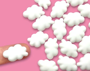 May include: A collection of white cloud-shaped charms on a pink background. The charms are small and have a smooth, rounded surface.